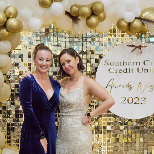 Tara Armbruster and Jasmine Wark posing in front of an glod backdrop with the text SCCU 2023 Awards Night